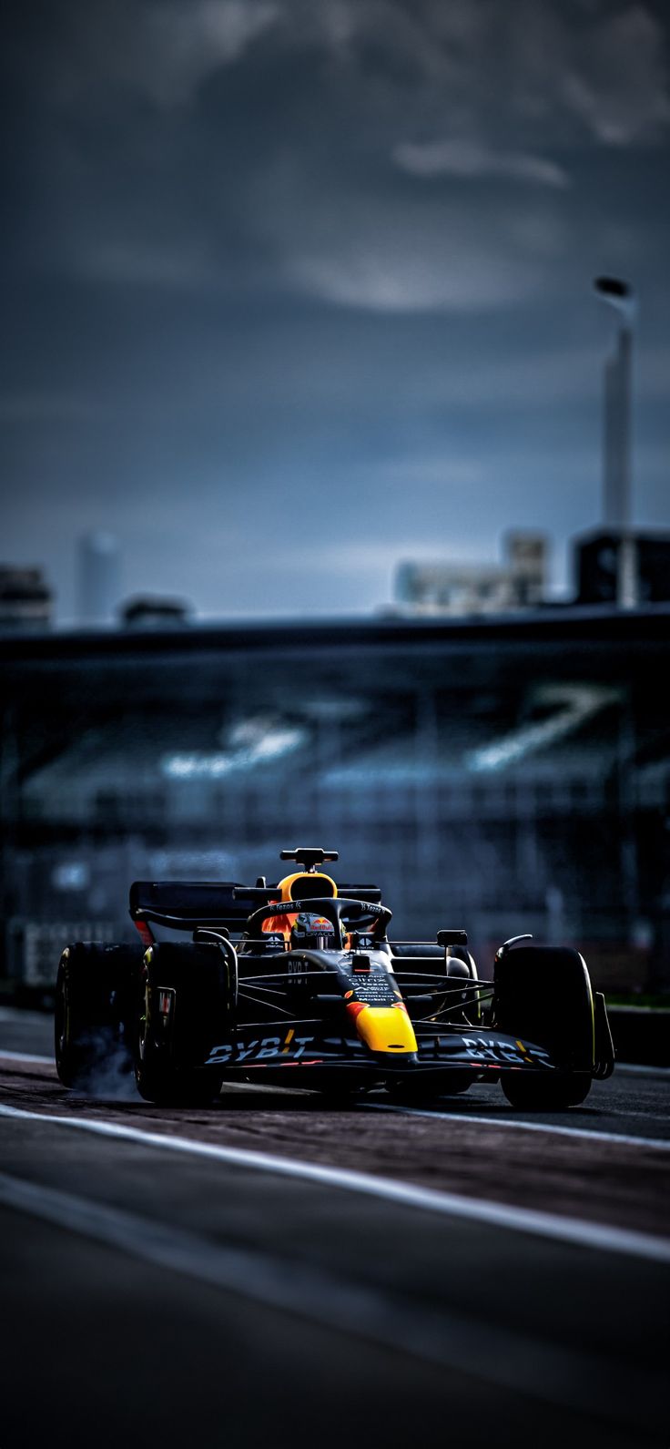 a yellow and black race car driving on a track with dark clouds in the background