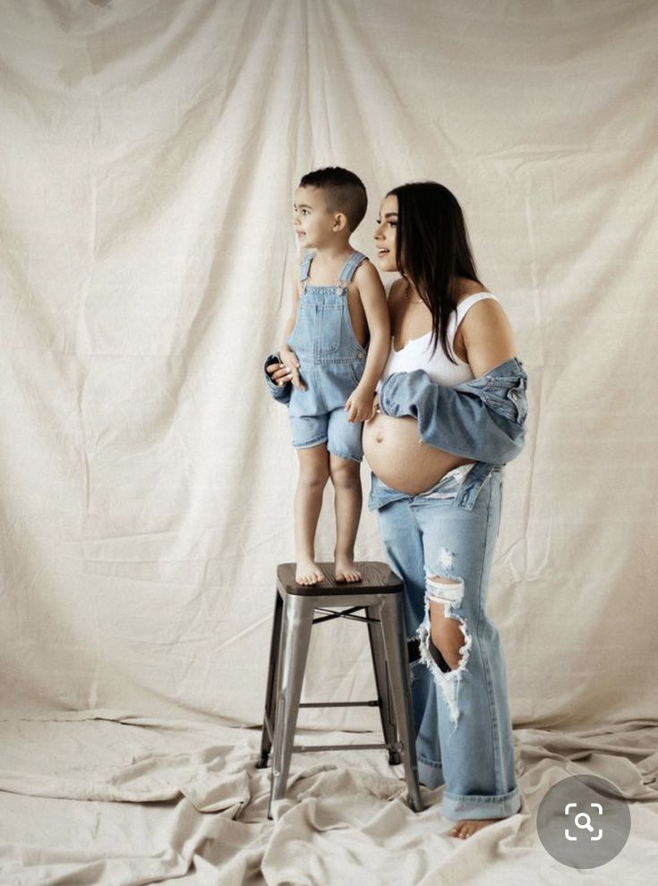 a pregnant woman standing on top of a stool next to a little boy wearing overalls