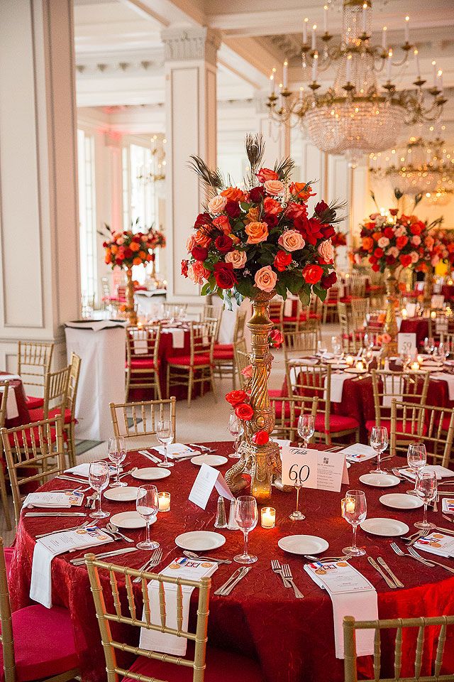 a table set with red linens, gold chairs and centerpieces for an elegant wedding reception