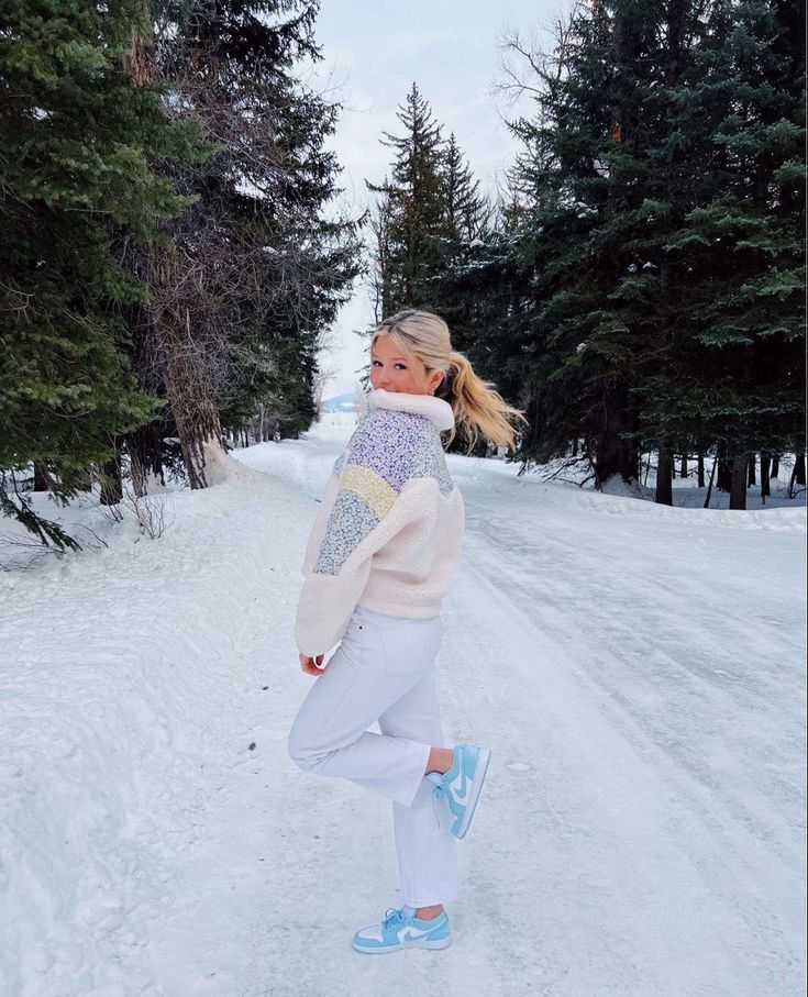 a woman is walking in the snow with her feet on the ground and trees behind her