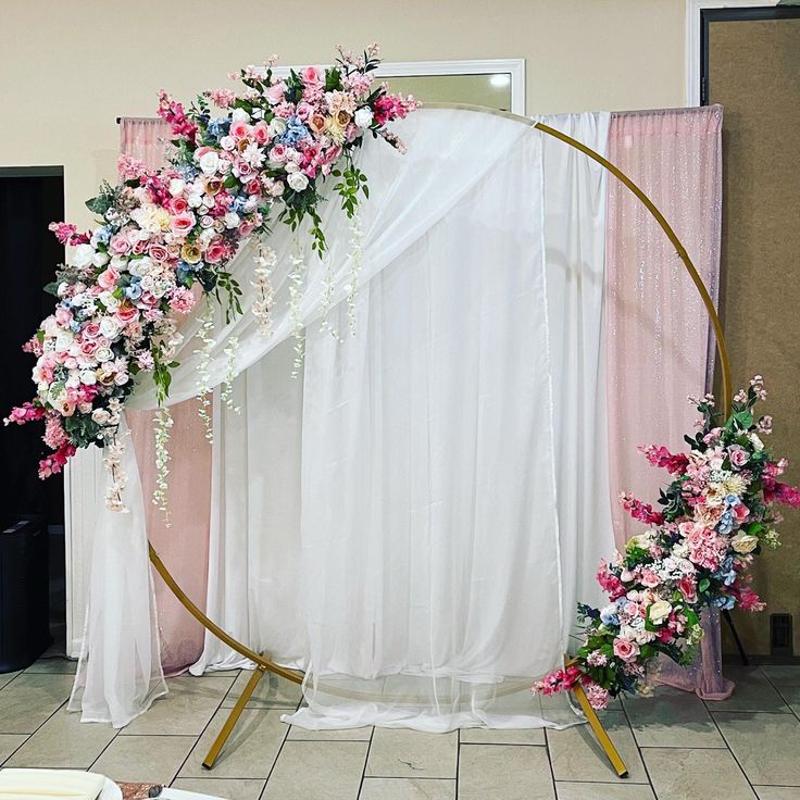 a wedding arch decorated with pink and white flowers on the floor in front of curtains