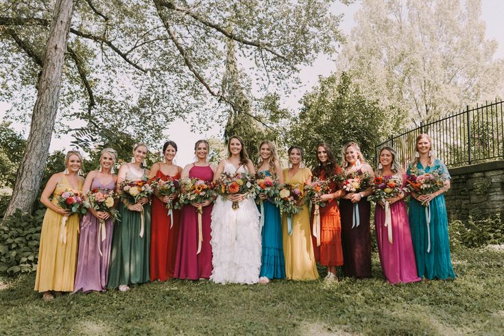 a group of women standing next to each other holding bouquets in front of a tree