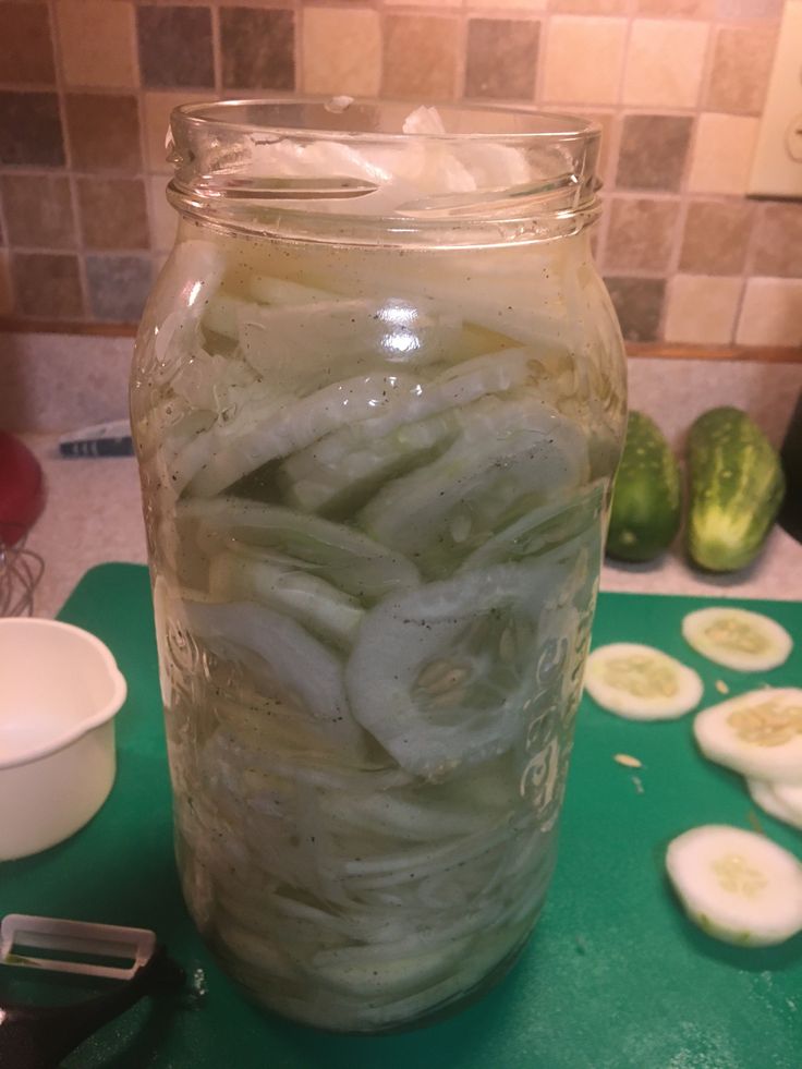 a jar filled with pickles sitting on top of a green cutting board next to sliced cucumbers