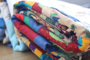 a stack of folded cloths sitting on top of a wooden floor next to a bed