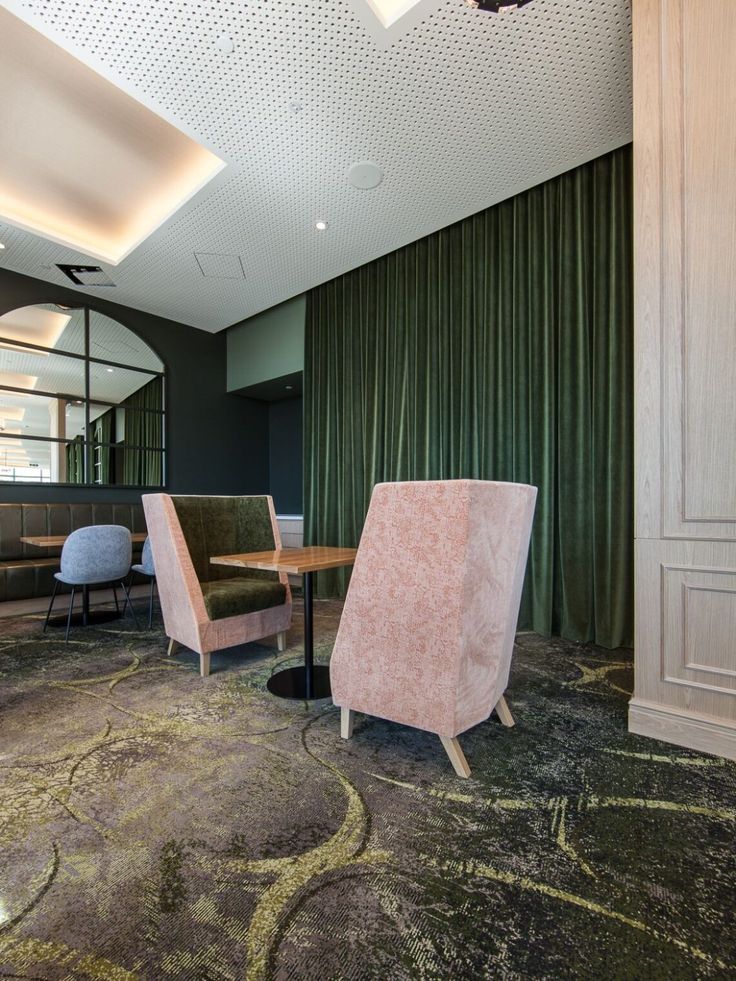 two pink chairs sitting next to each other on top of a carpeted floor in front of a green curtain