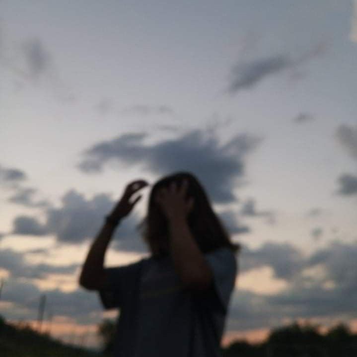 a person standing in front of a cloudy sky with their hands up to their face