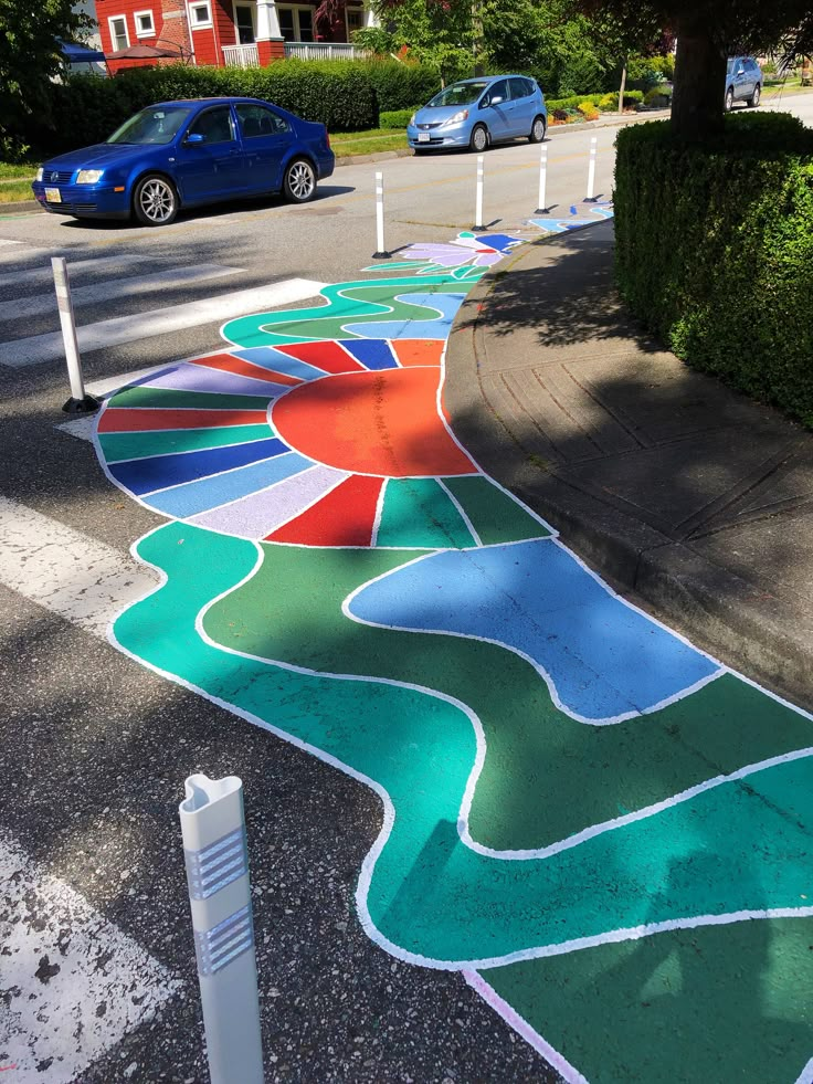 a sidewalk painted with different colors and shapes on the side of a road next to a blue car