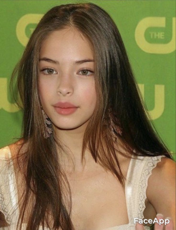 a woman with long hair wearing a white top and holding her hand out to the side