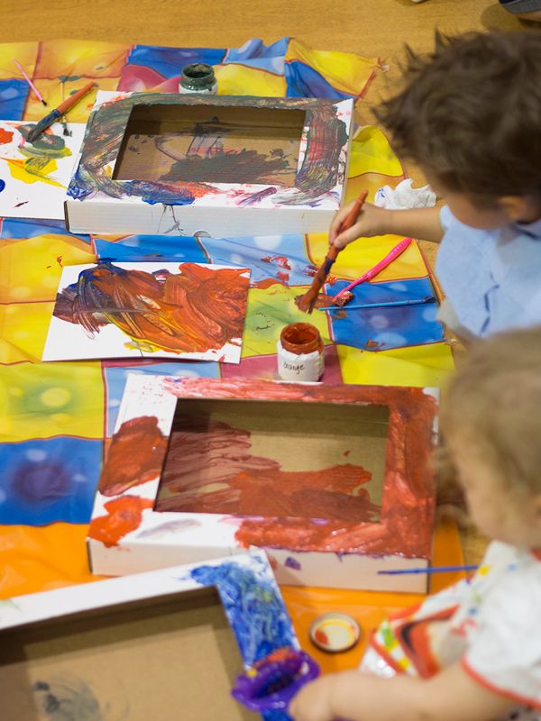 two children are painting on paper with paintbrushes and watercolors in front of them