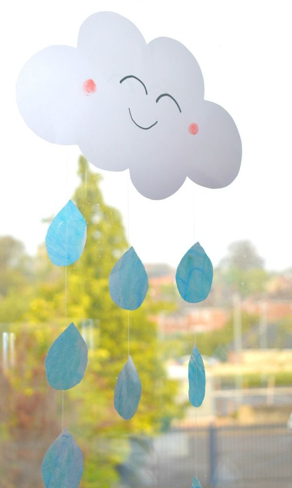 a paper cloud with rain drops hanging from it's side, in front of a window