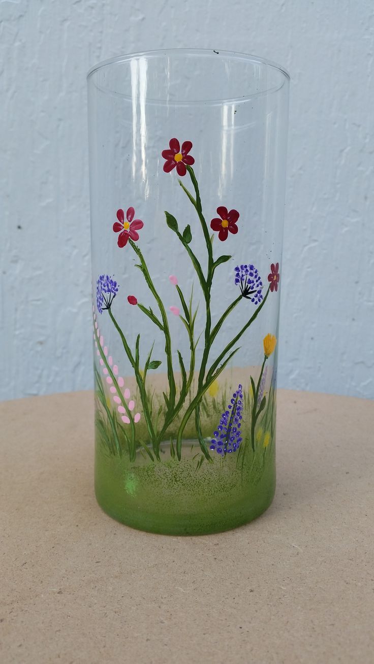 a glass with flowers painted on it sitting on a table