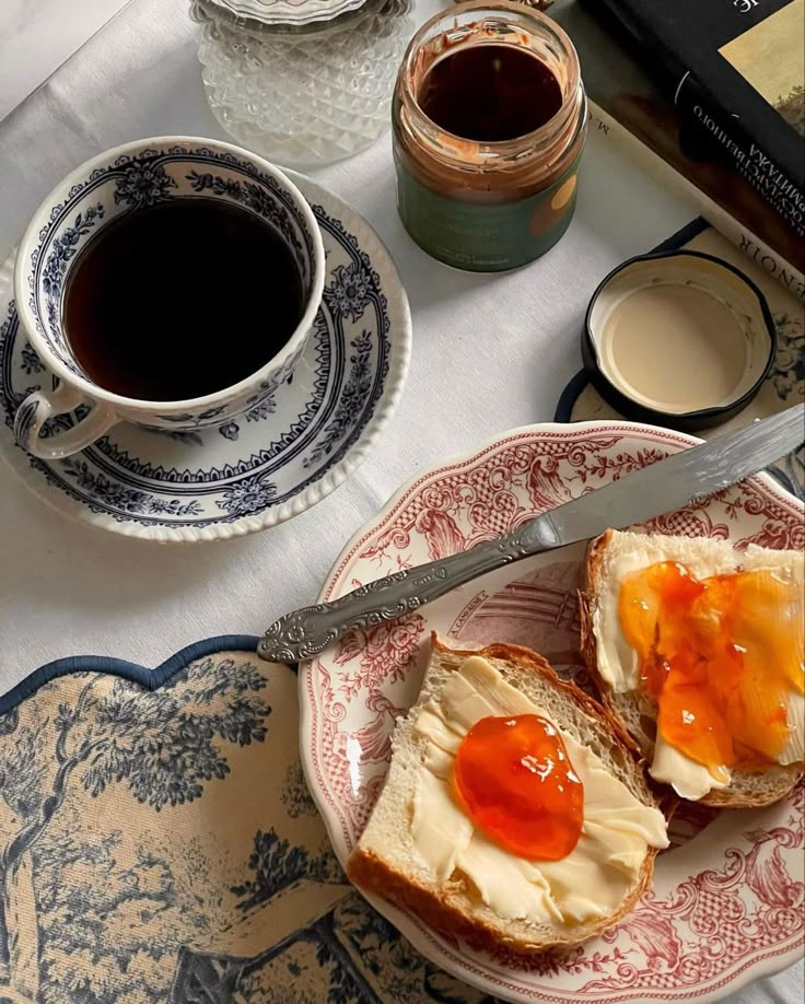 two pieces of bread with jam on them sitting on a plate next to a cup of coffee