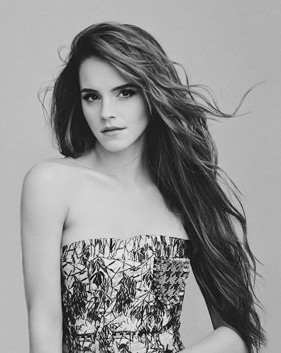 a woman with long brown hair standing in front of a pink wall wearing a strapless top