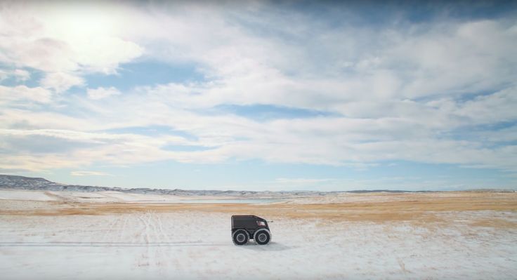 a truck is driving through the snow in front of some hills and clouds on a sunny day