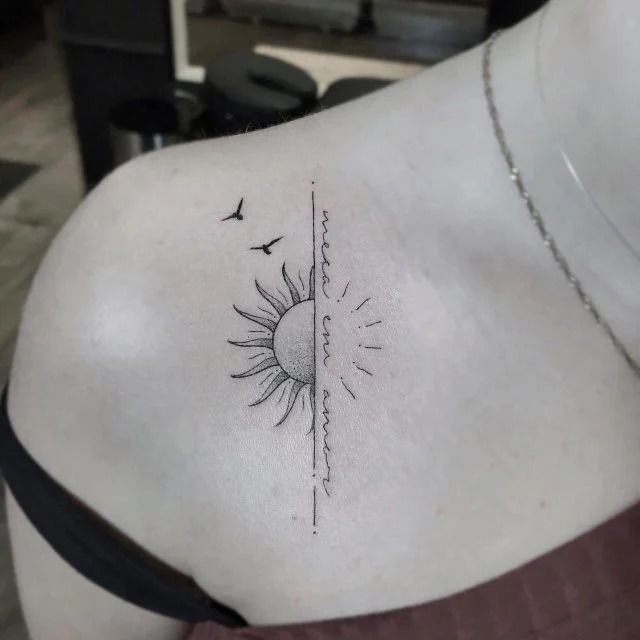 the back of a woman's shoulder with a sun and birds tattoo on it