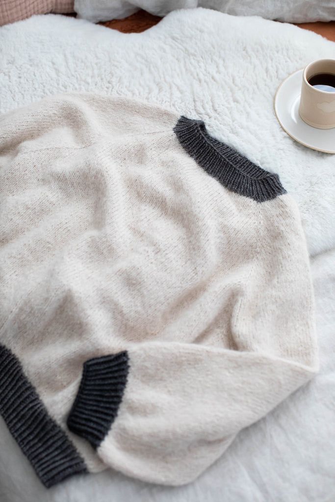 a cup of coffee sits on top of a white blanket next to a black and grey sweater