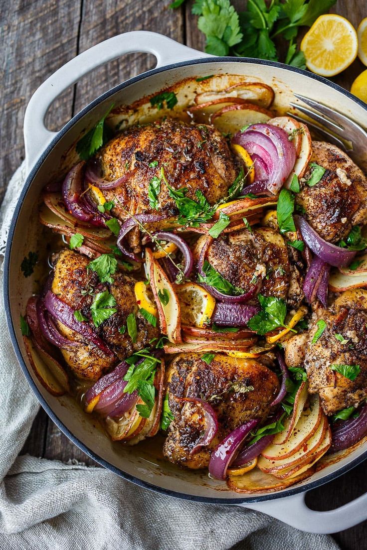 a pan filled with meat and onions on top of a wooden table next to lemons