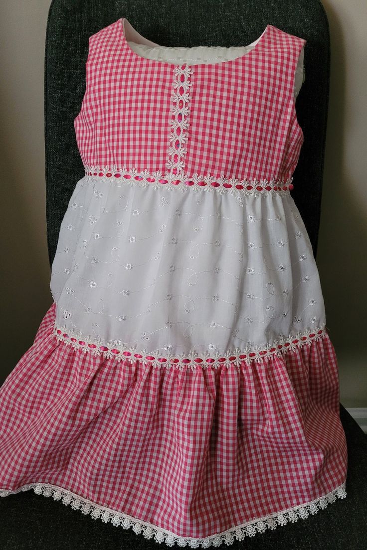 Pink gingham and white eyelet 100% cotton fabrics. Two tiers ruffle skirt. Insertion trim with pink ribbon connect bodice and skirt and the tiers. Lace trim in hem. White Lace Trim Dress For Picnic, Summer Gingham Dress With Tiered Skirt, White Ruffle Hem Dress For Picnic, Gingham Tiered Ruffle Dress, Gingham Tiered Dress With Ruffles, Plaid Cotton Tiered Dress, Cotton Lace Trim Dress For Picnic, Cotton Gingham Dress With Ruffle Hem, Gingham Cotton Dress With Ruffle Hem