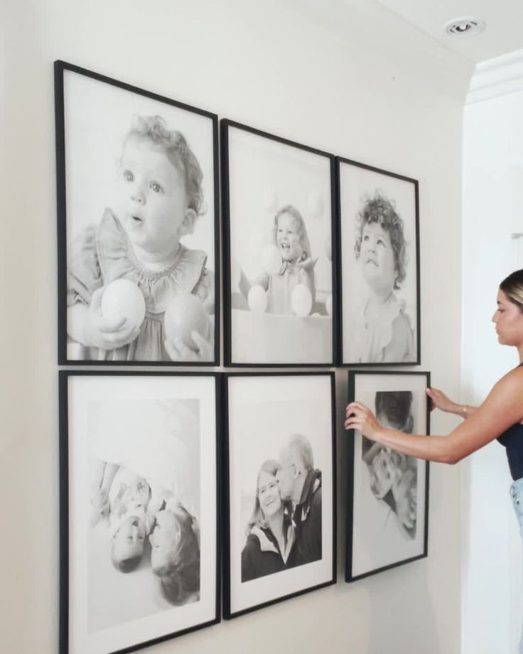 a woman hanging pictures on the wall with her baby's face in black and white