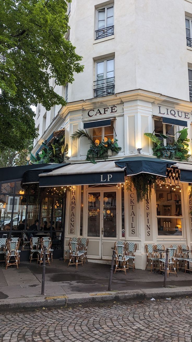 an outdoor cafe with tables and chairs on the sidewalk in front of a white building