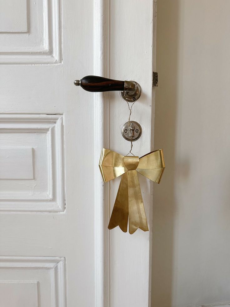 a door handle with a gold bow hanging from it's side next to a white door