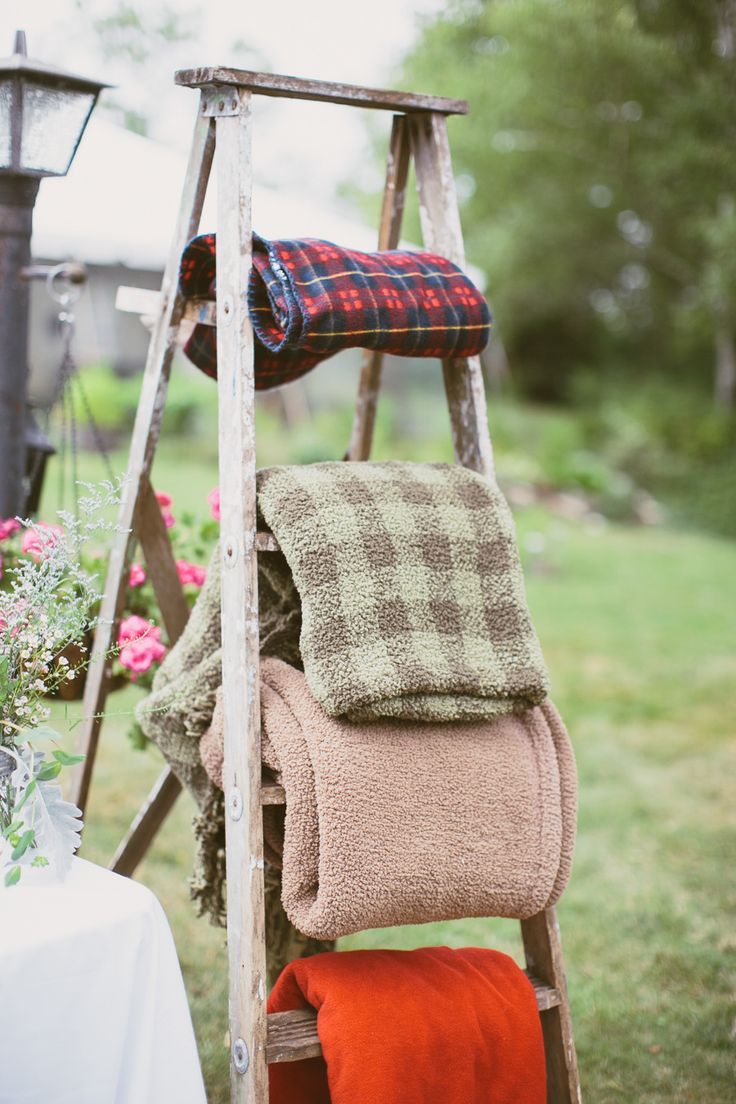 an old ladder with blankets on it and flowers in the back ground near a table