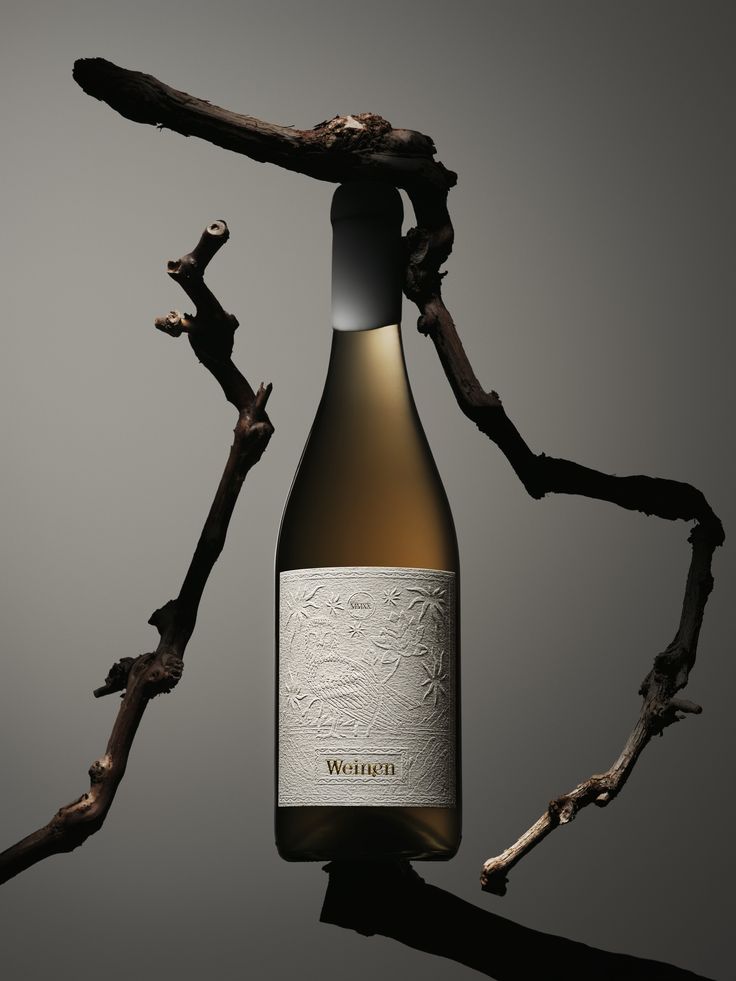 a bottle of wine sitting on top of a wooden branch next to a twig