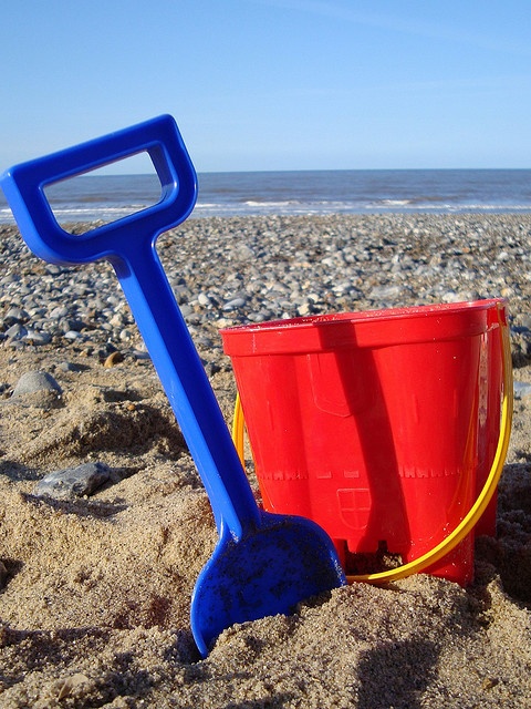 a red bucket and blue shovel sitting in the sand