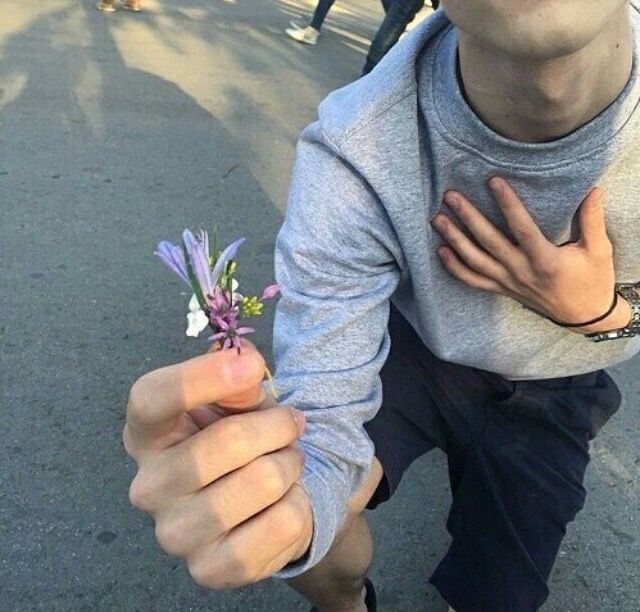 a man holding a small purple flower in his right hand