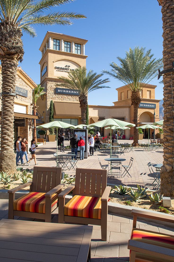 two wooden chairs sitting next to each other on a sidewalk near palm trees and buildings