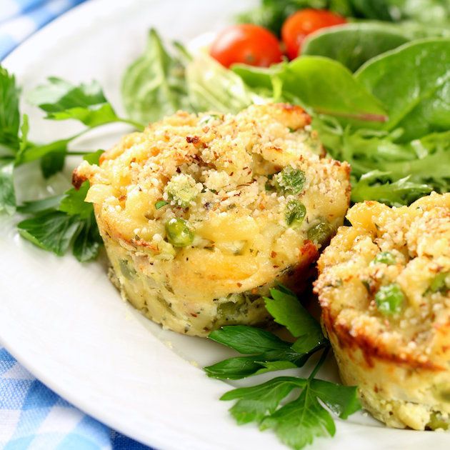 two muffins on a plate with greens and tomatoes