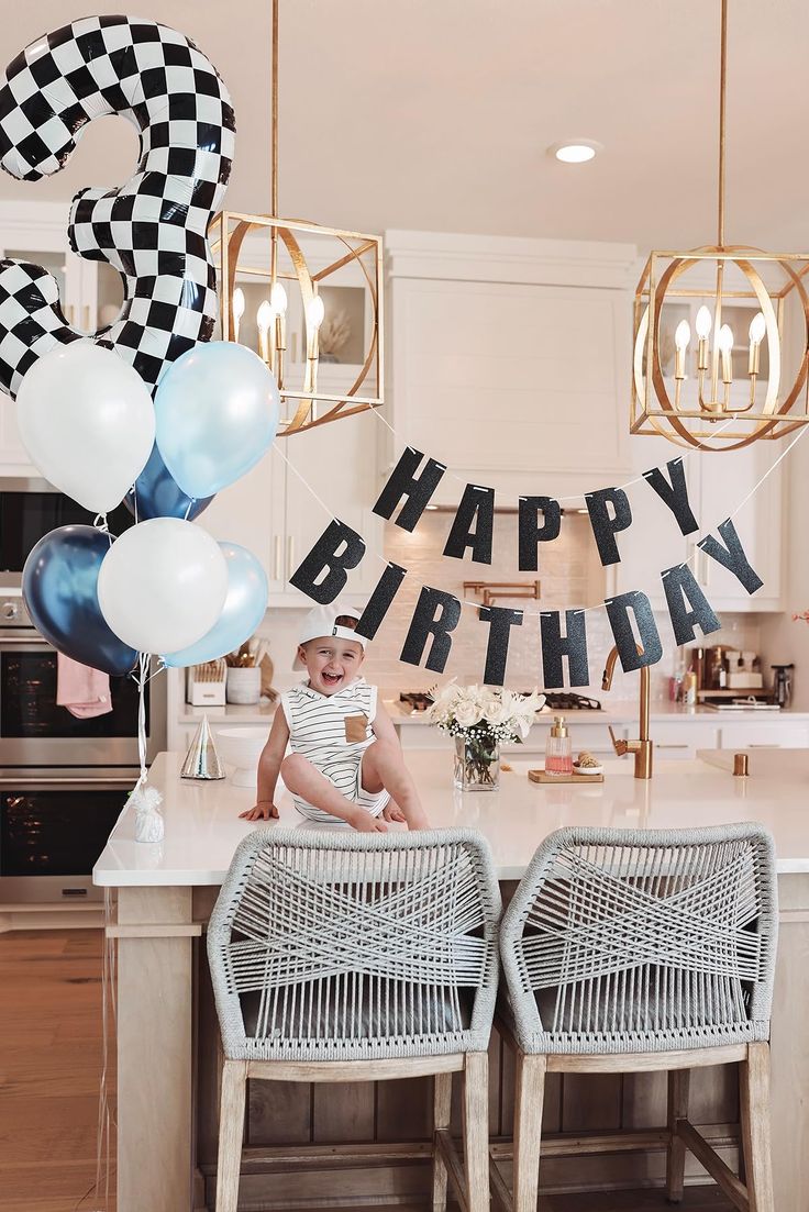 a baby sitting on top of a kitchen counter next to balloons