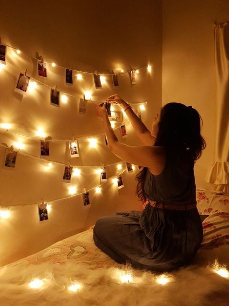 a woman sitting on top of a bed next to a wall covered in pictures and lights