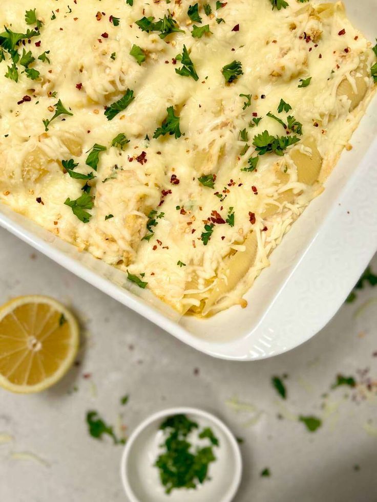 a casserole dish with cheese and parsley on top, next to a lemon slice