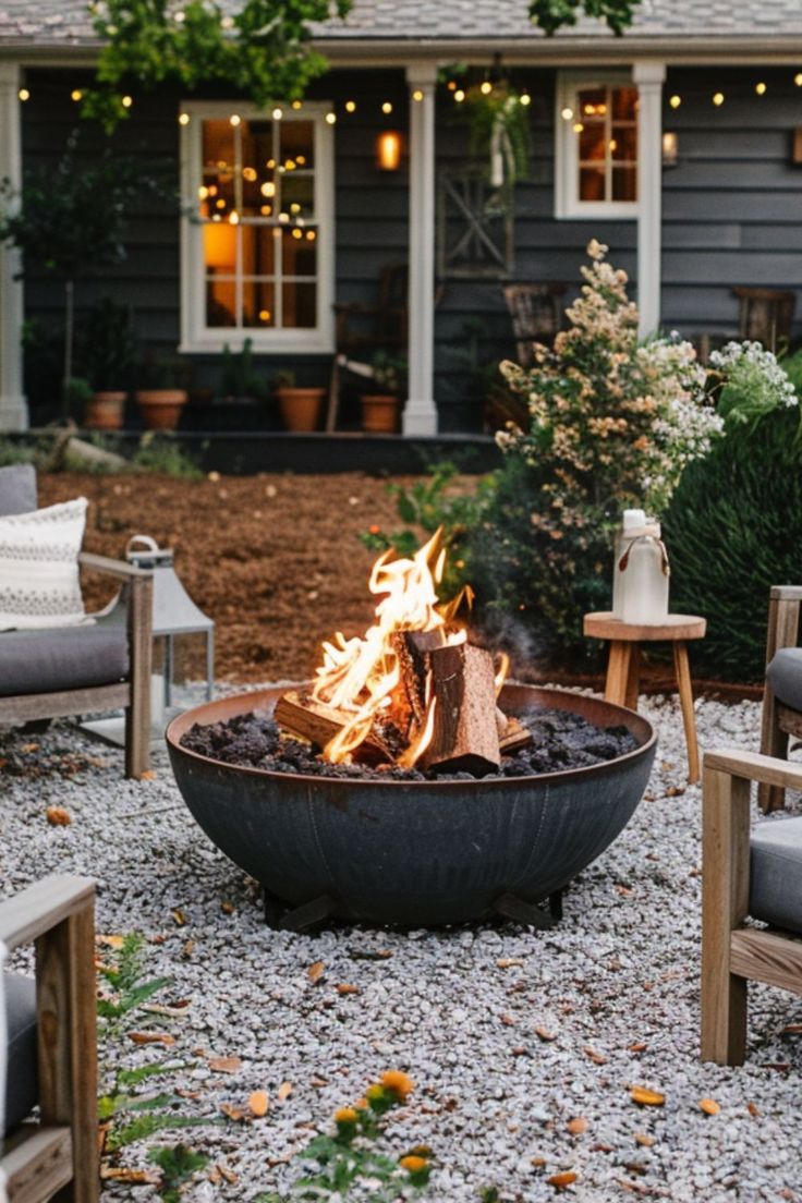 a fire pit sitting in the middle of a gravel covered yard with chairs around it