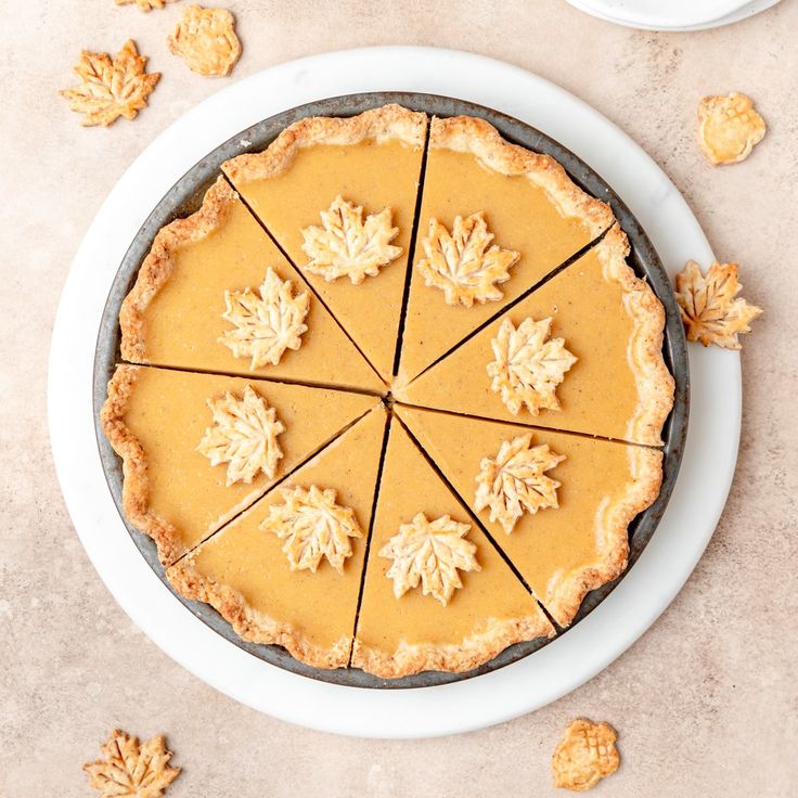 a pie with four slices cut out on a white plate next to some leaves and nuts