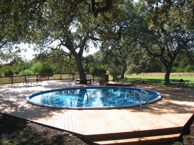 an above ground pool surrounded by wooden decking and benches in the middle of a grassy area