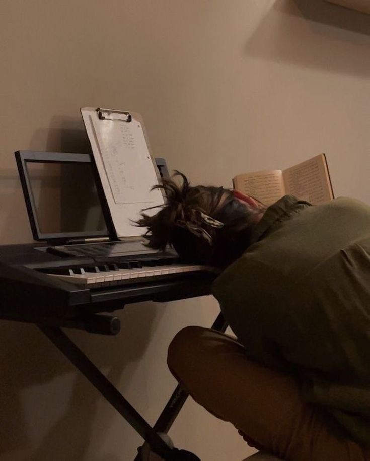 a person laying their head on top of a keyboard with an open book next to it