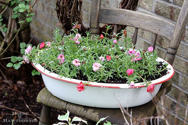 a planter filled with pink flowers sitting on top of a wooden chair next to a brick wall