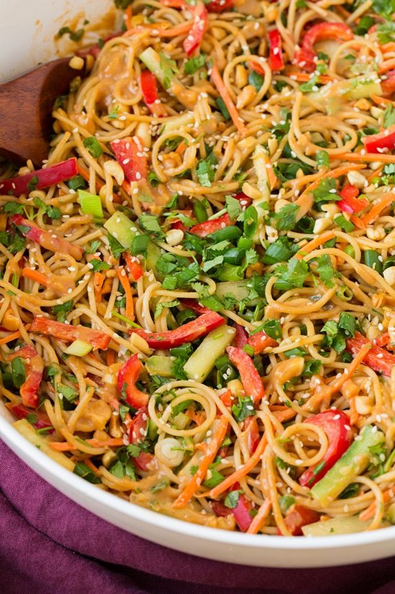 a bowl filled with noodles and vegetables on top of a purple cloth next to a wooden spoon