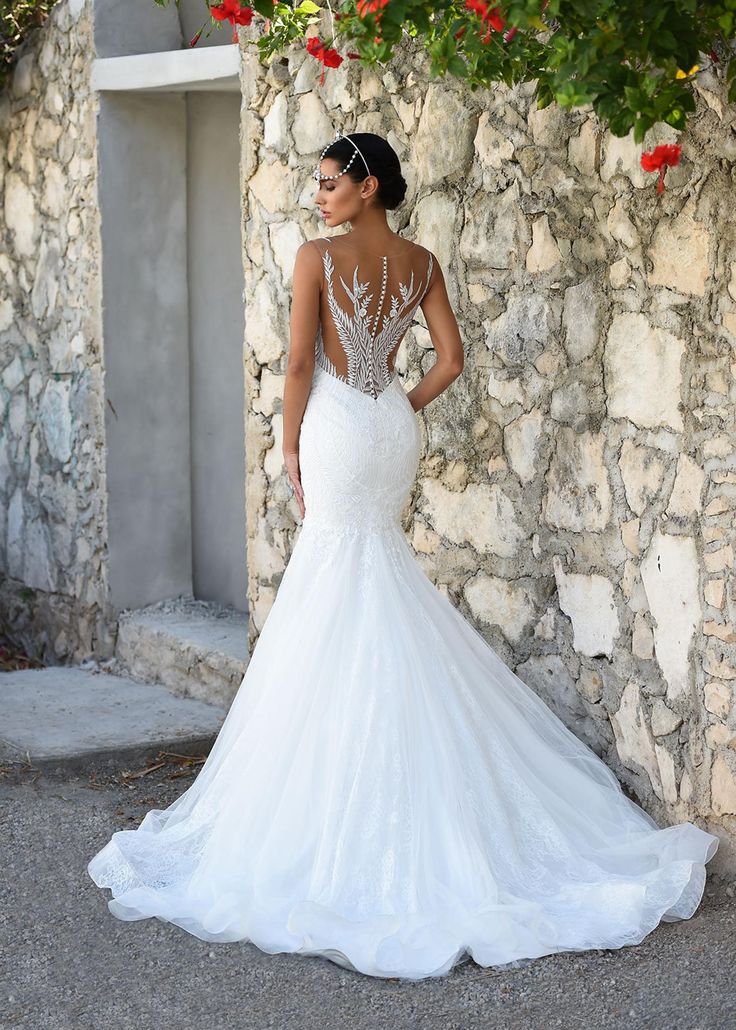 a woman in a wedding dress standing next to a stone wall with flowers on it