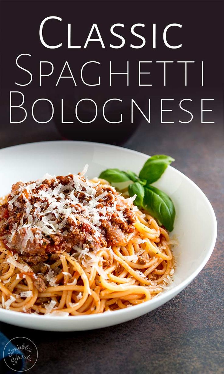 a white plate filled with spaghetti and sauce on top of a wooden table next to a green leafy garnish