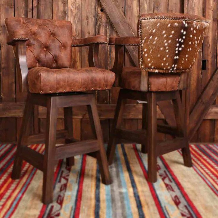 two brown leather chairs sitting next to each other on top of a striped rug in front of a wooden wall