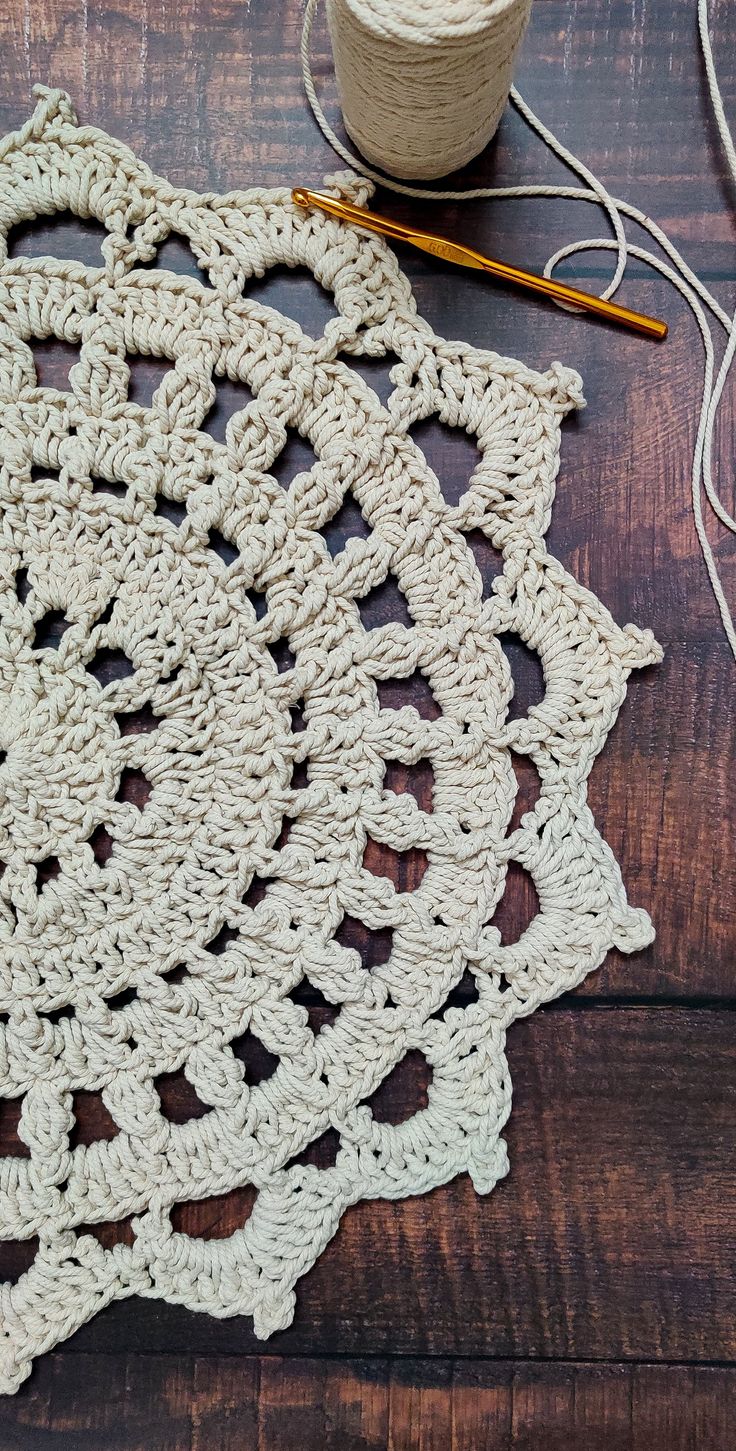 crocheted doily on wooden table with yarn and scissors