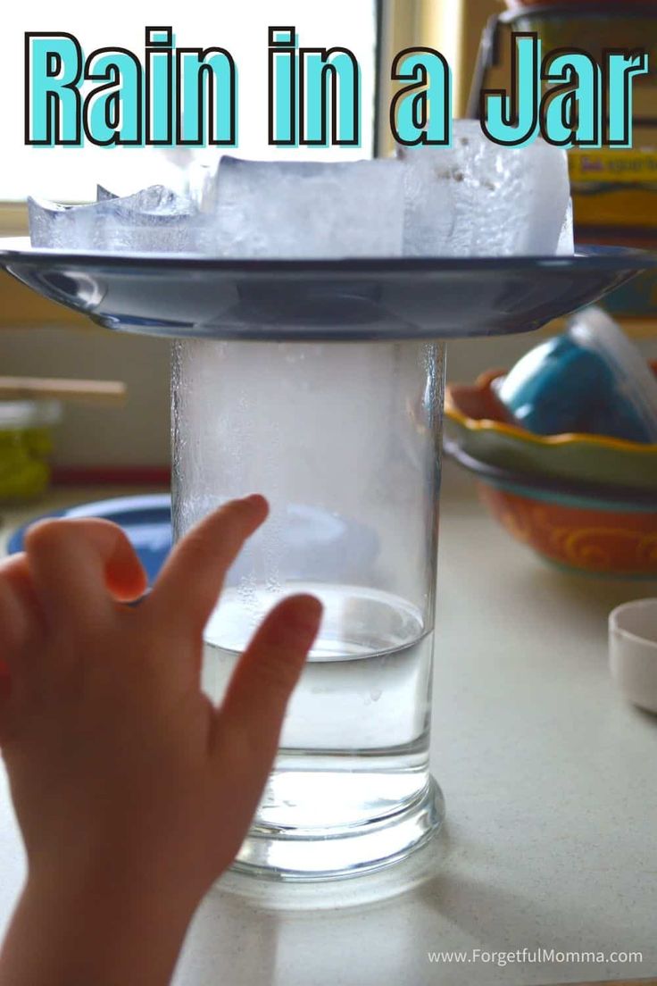 a hand is pointing at an ice cube in a glass on a table with the words rain in a jar above it