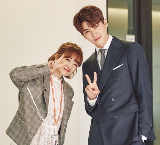 two people standing next to each other in front of a wall and one person is making the peace sign