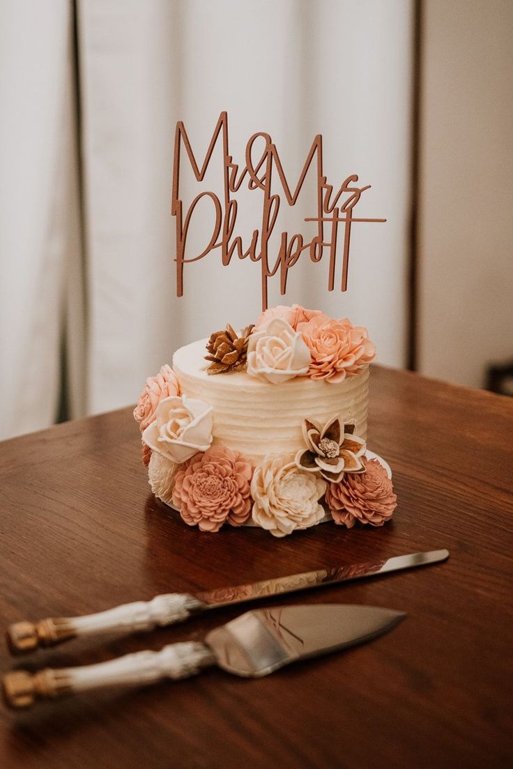 a wedding cake with flowers on top sits on a table next to a knife and fork