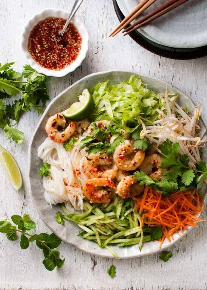 a white plate topped with shrimp and veggies next to chopsticks on a table