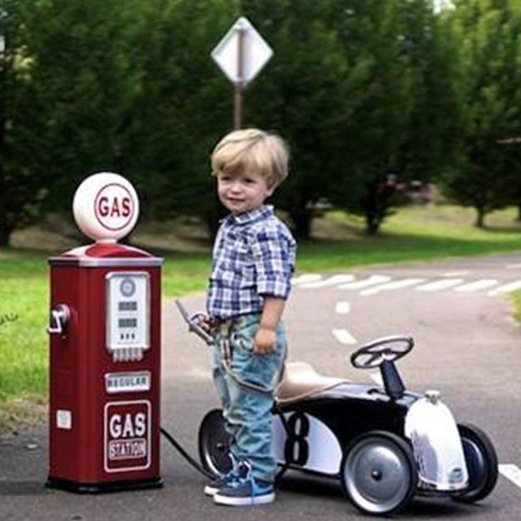 a young boy standing next to a toy car and gas pump on the side of a road