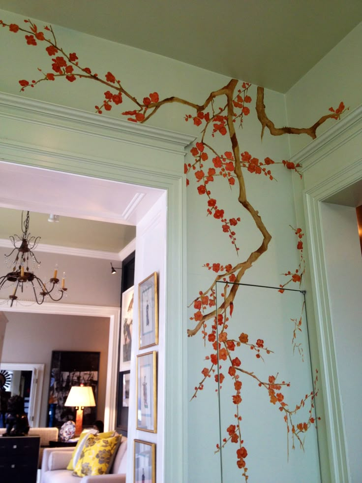 a living room with a tree painted on the wall next to a couch and chandelier